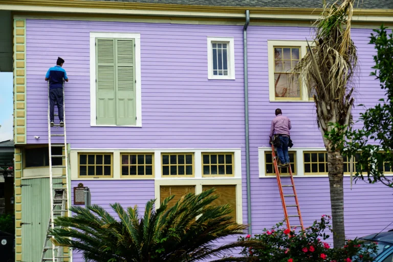 Two painters on ladders working on an exterior wall